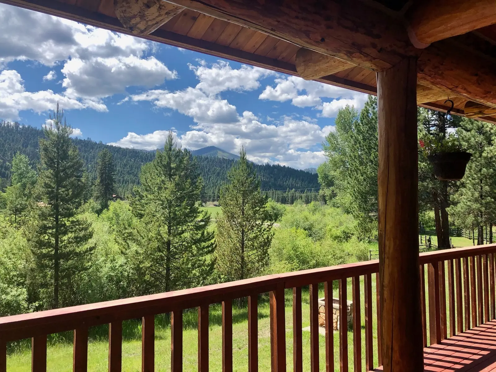 The view from a covered cabin porch over the pines to the mountains