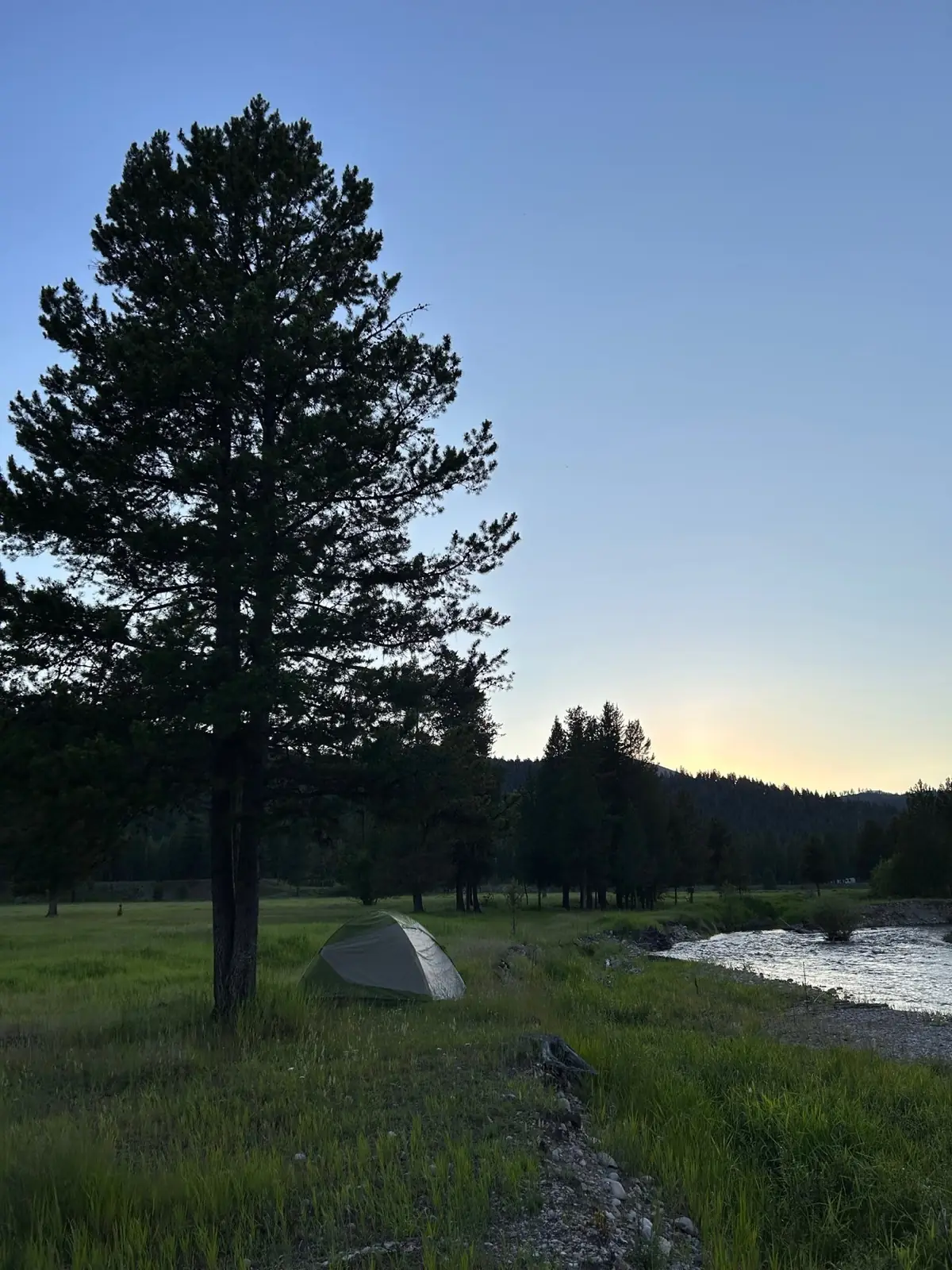 A tent pitched in the meadow by the river at dusk