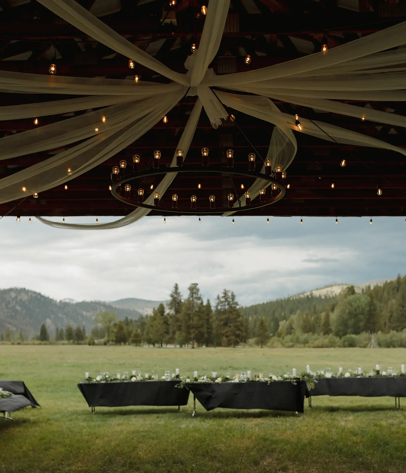 Draped fabric and string lights under the hangar roof at Alta Ranch, above reception tables