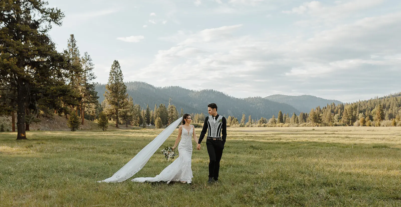 A bride and groom walking across the wide green meadow toward the mountains at Alta Ranch