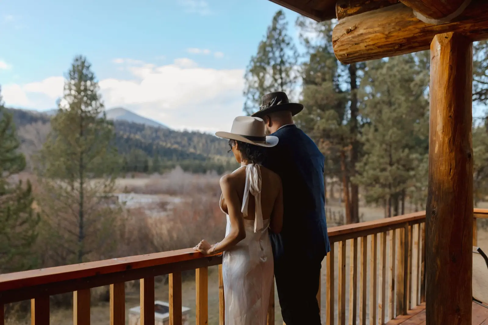 A couple in cowboy hats leaning on the lodge deck rail, looking out over the river and valley