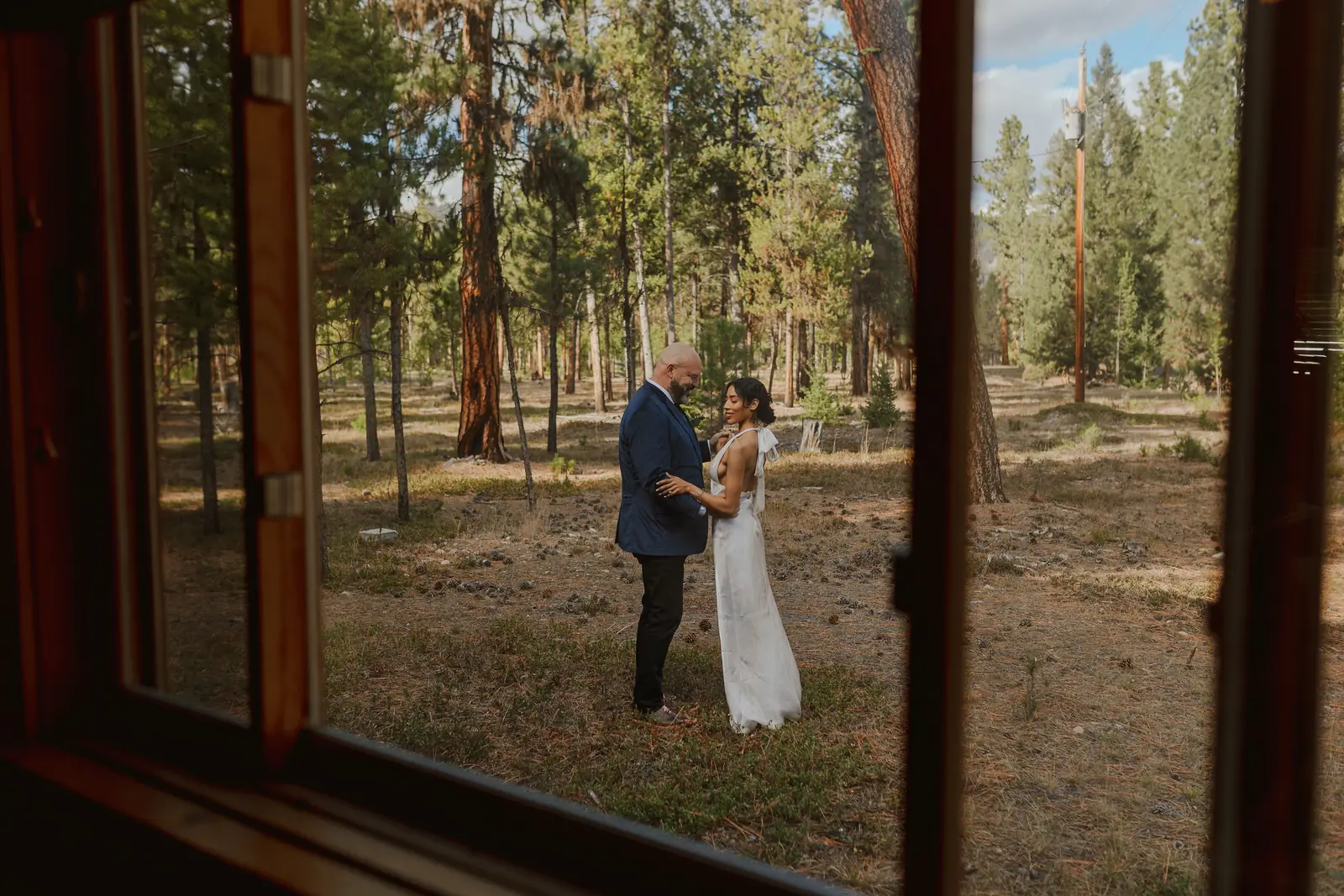 A couple embracing in the pines, seen through a cabin window