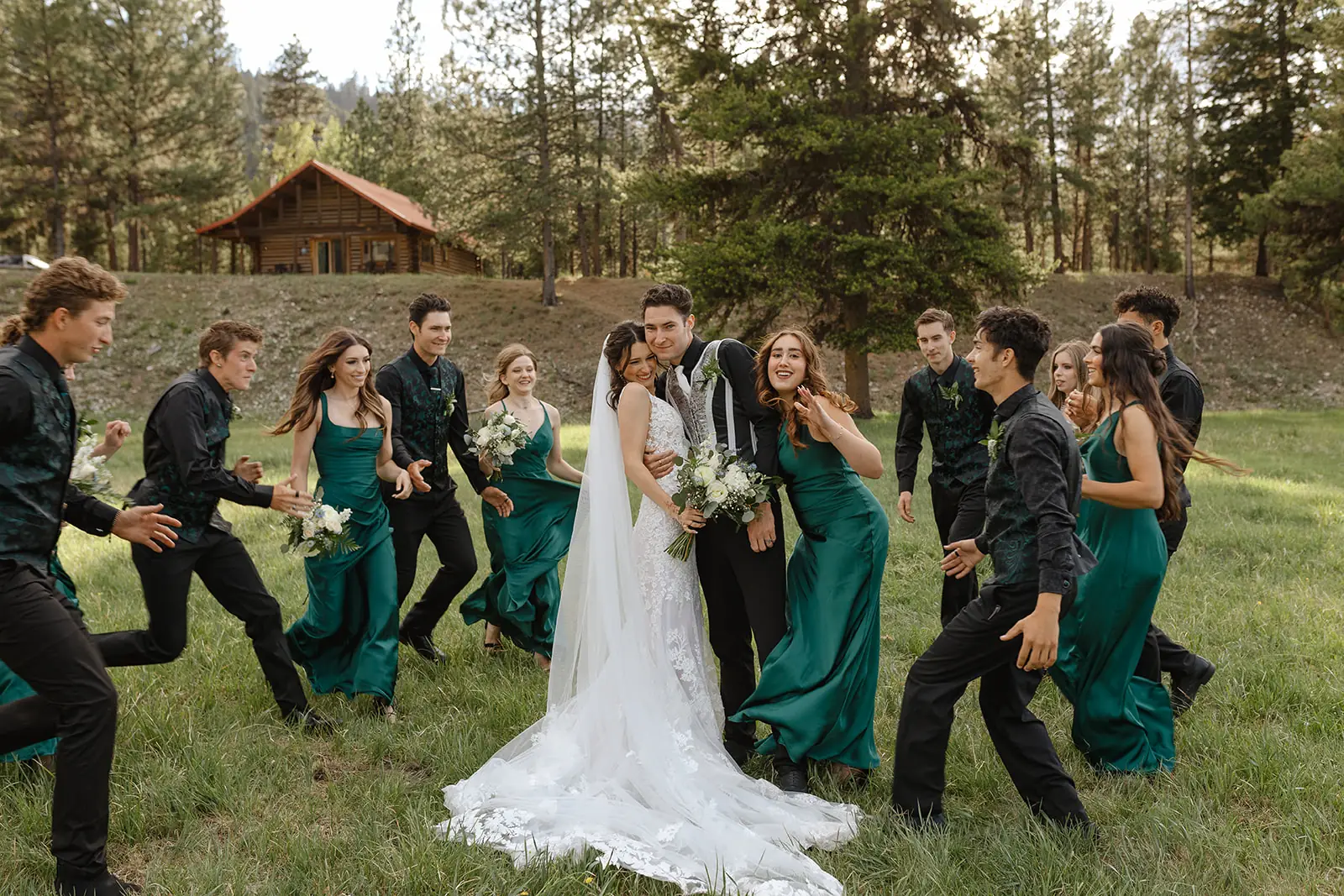The wedding party celebrating in the meadow with a cabin behind them