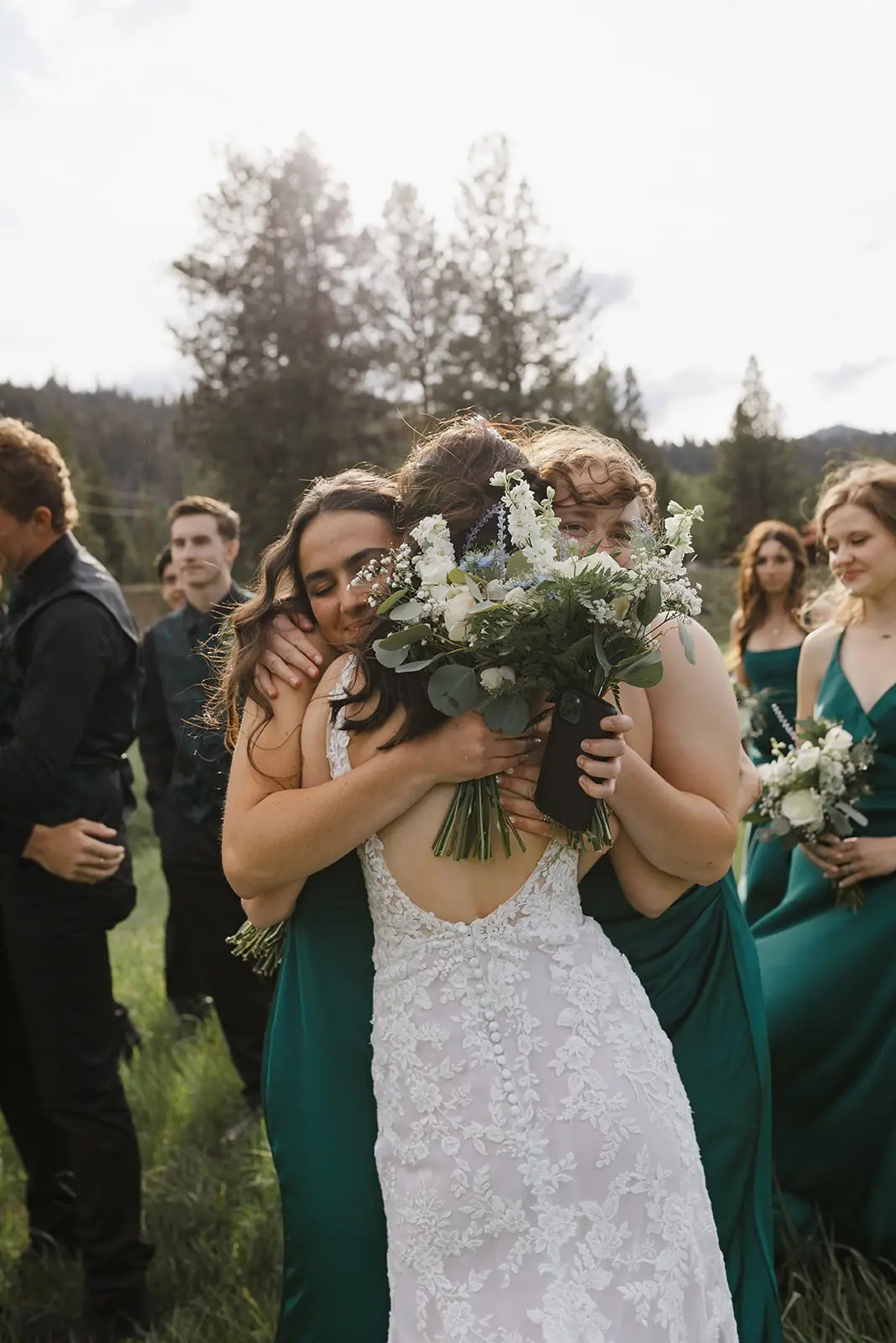 A bride hugging her bridesmaids in green dresses among the pines