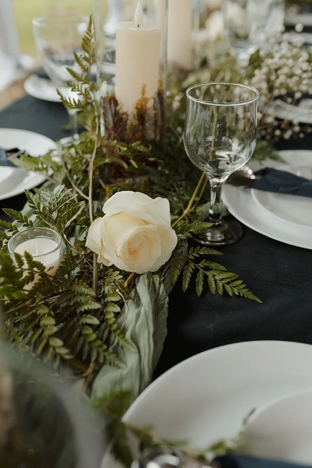 A white rose and greenery centerpiece with glassware on a reception table