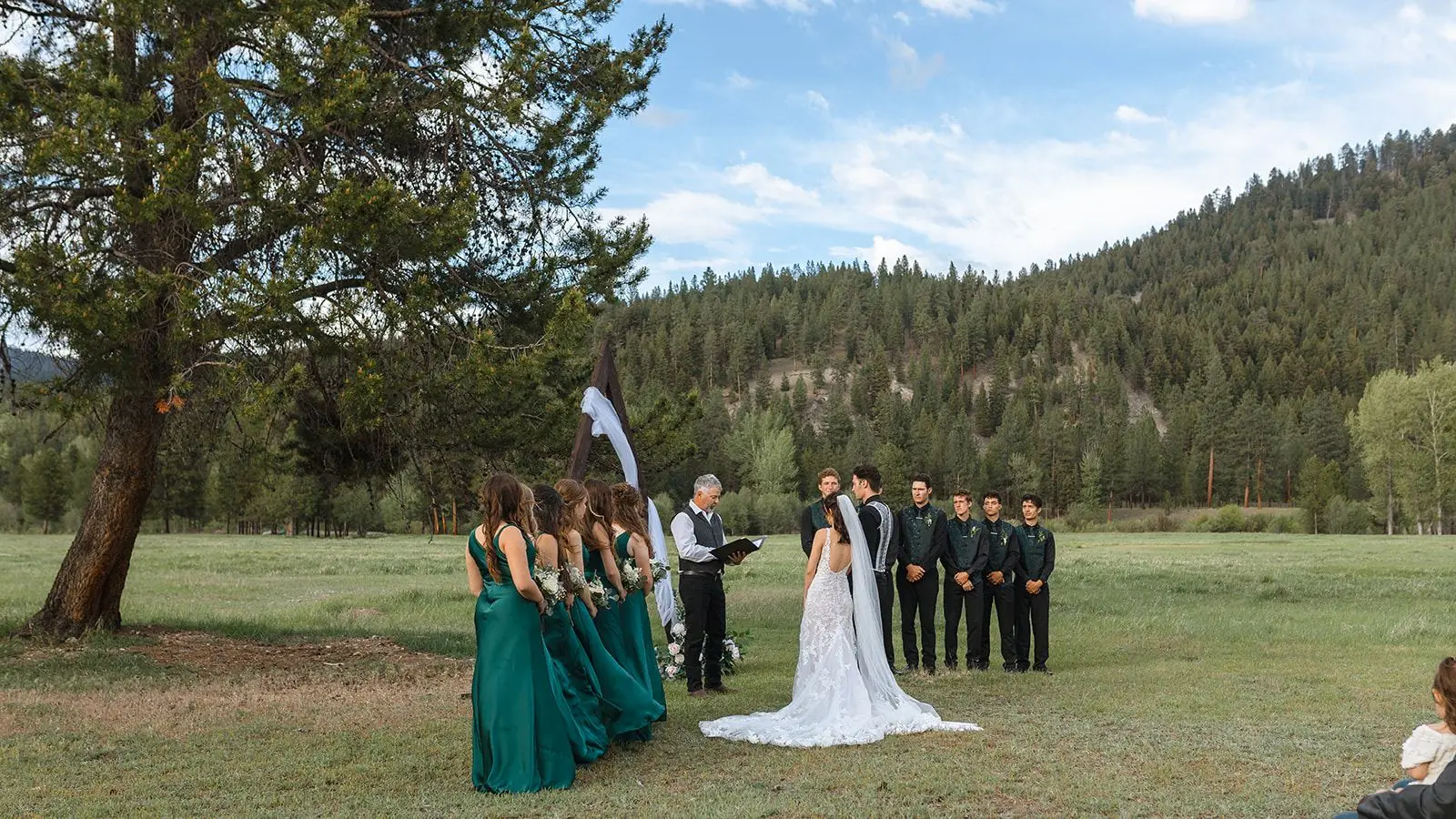 A couple exchanging vows in the open meadow with ponderosa pine and mountains behind them at Alta Ranch near Darby, Montana