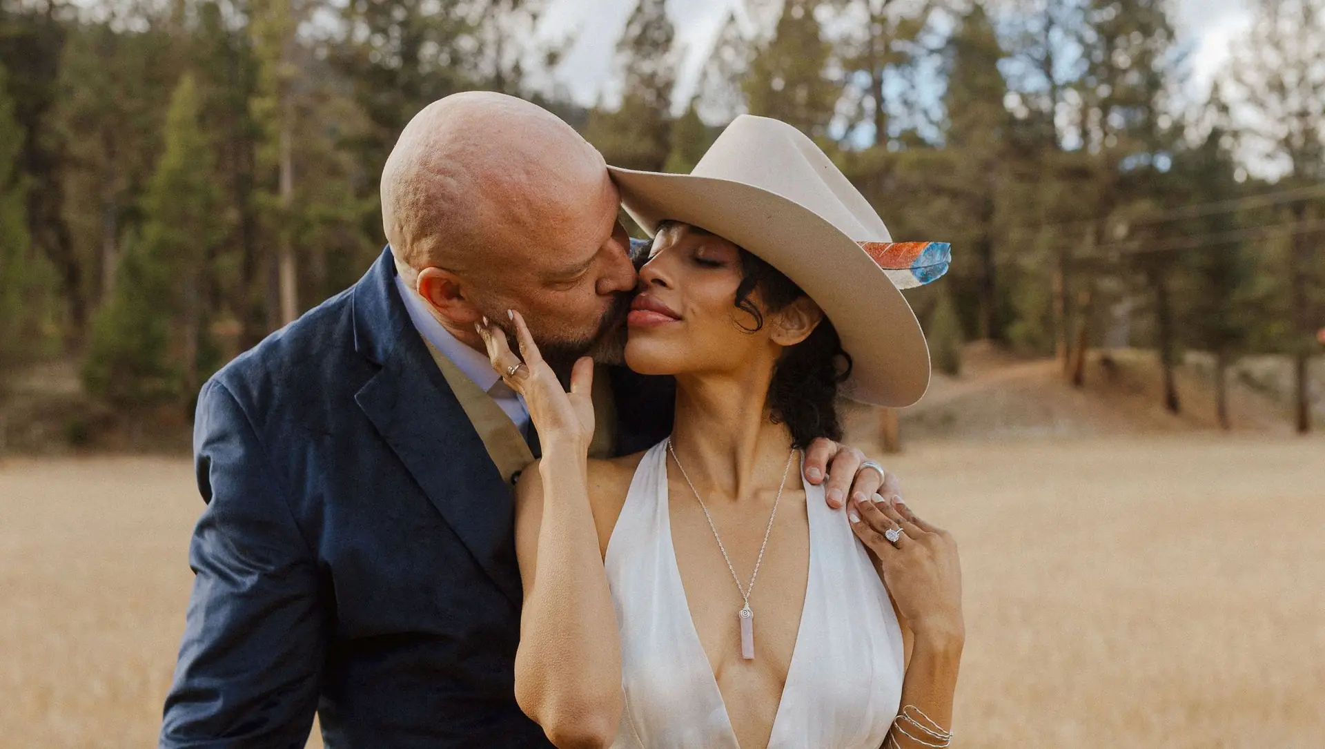 A couple in a cowboy hat sharing a kiss in the golden meadow