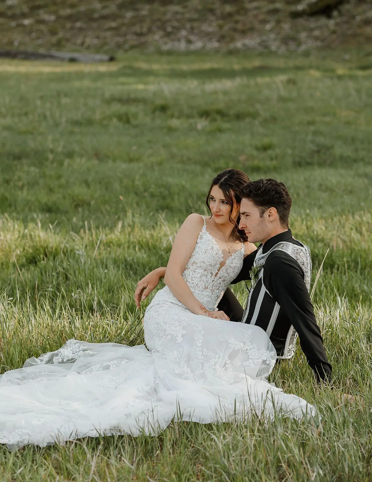 A couple sitting together in the tall green grass at golden hour at Alta Ranch
