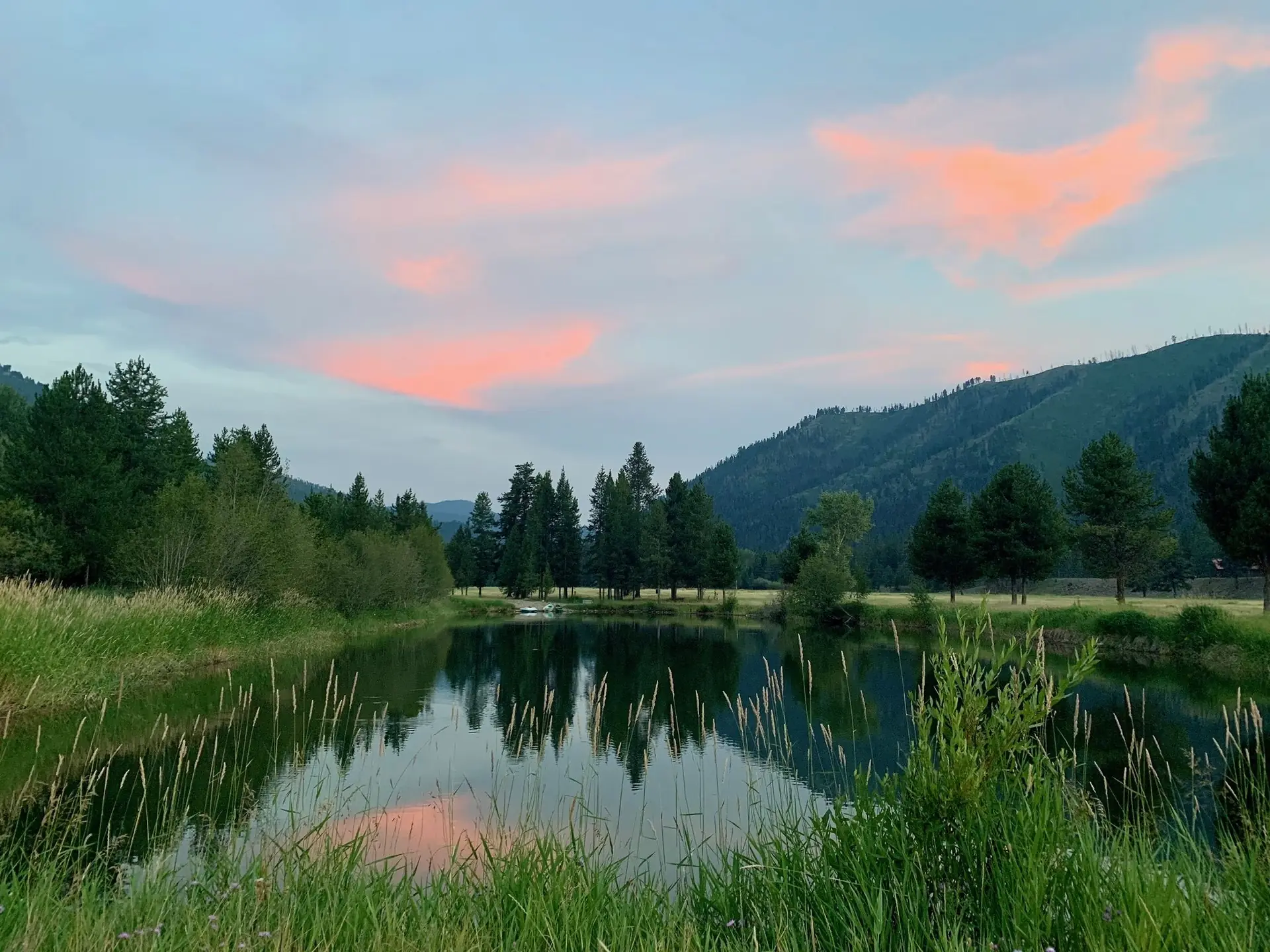 The ranch trout pond reflecting a pink evening sky below the mountains