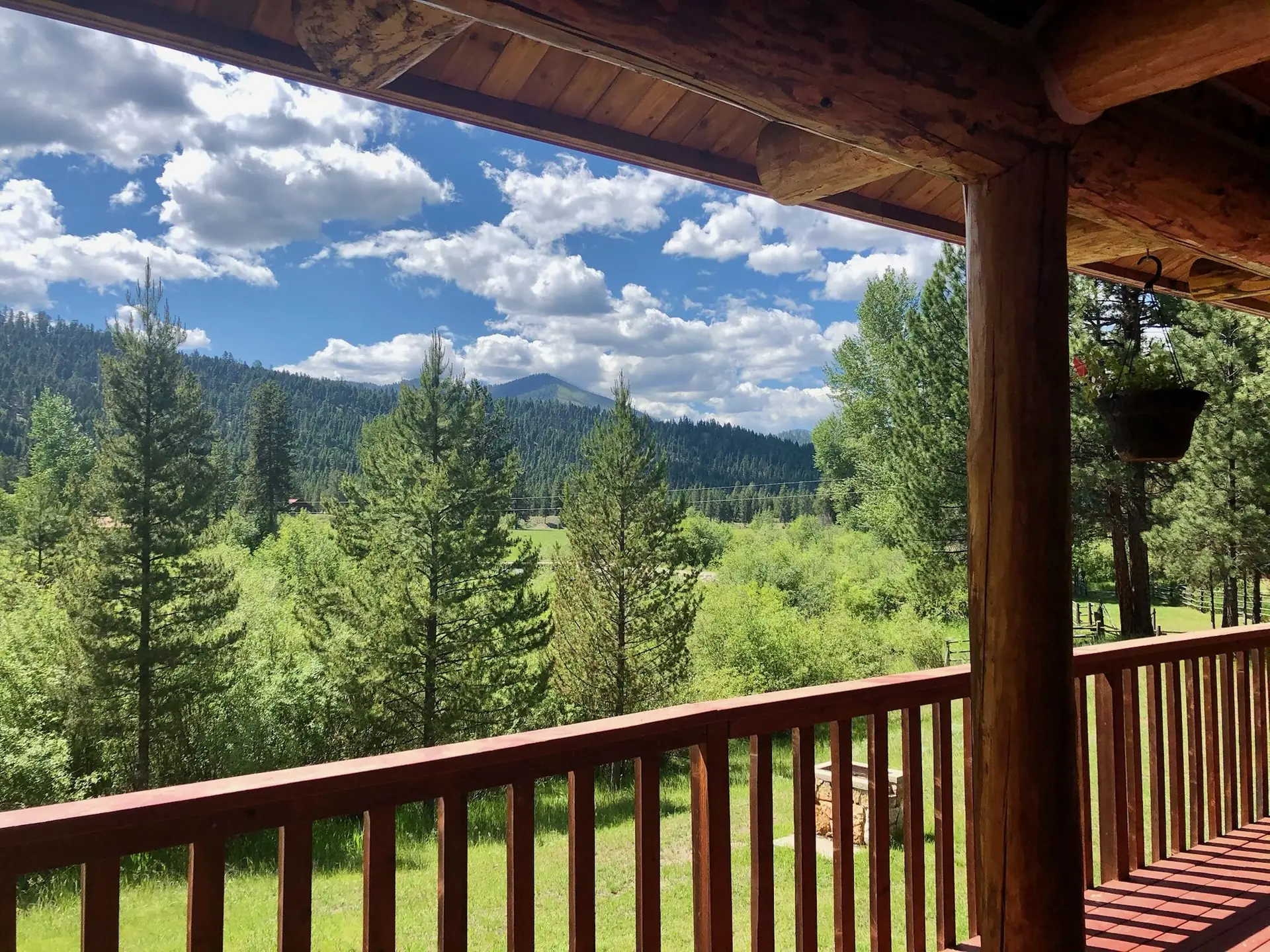 The view from a log cabin porch over pines and meadow to the mountains