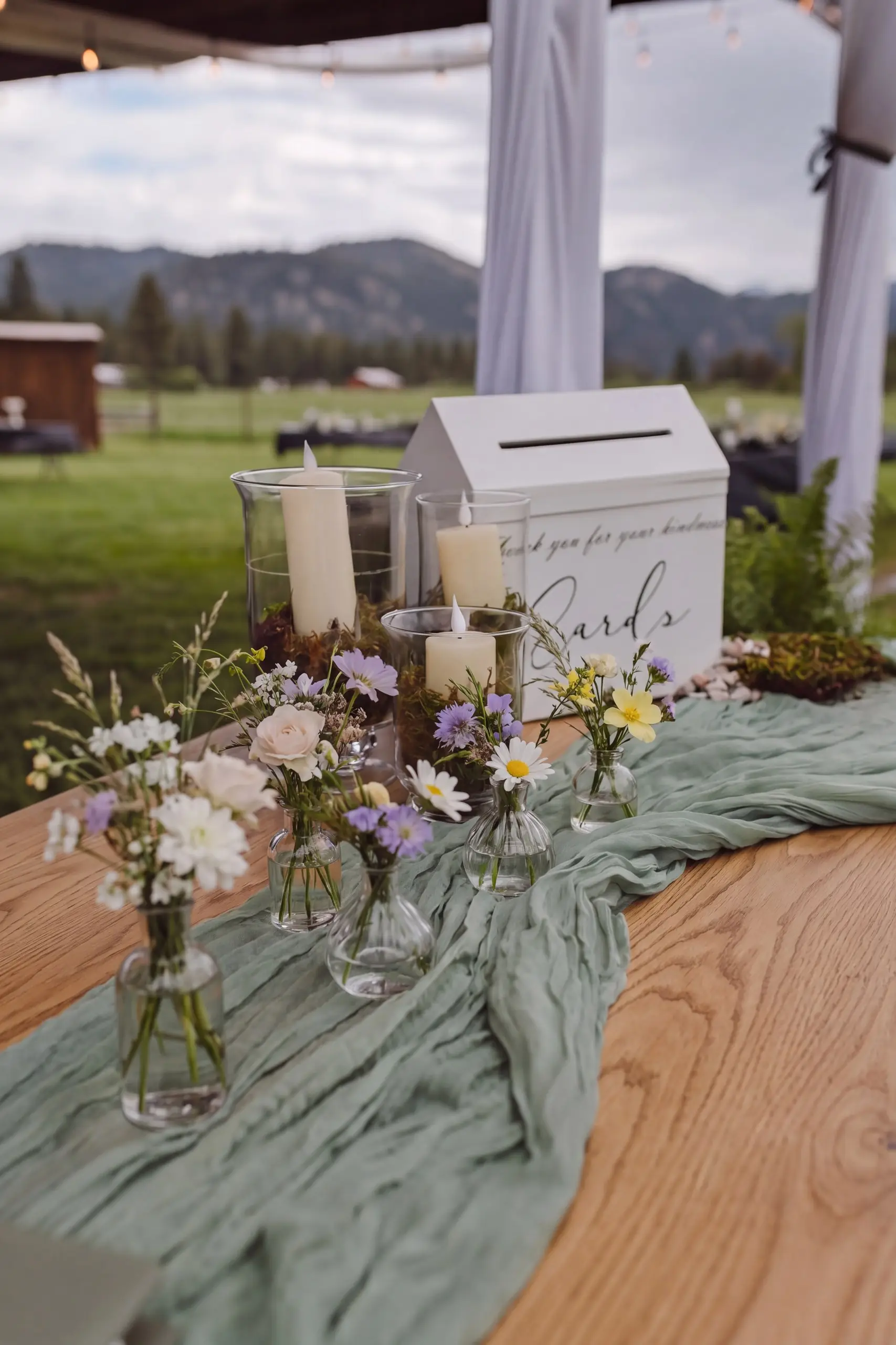 A card table with florals and a sage runner under the hangar, the meadow and mountains behind