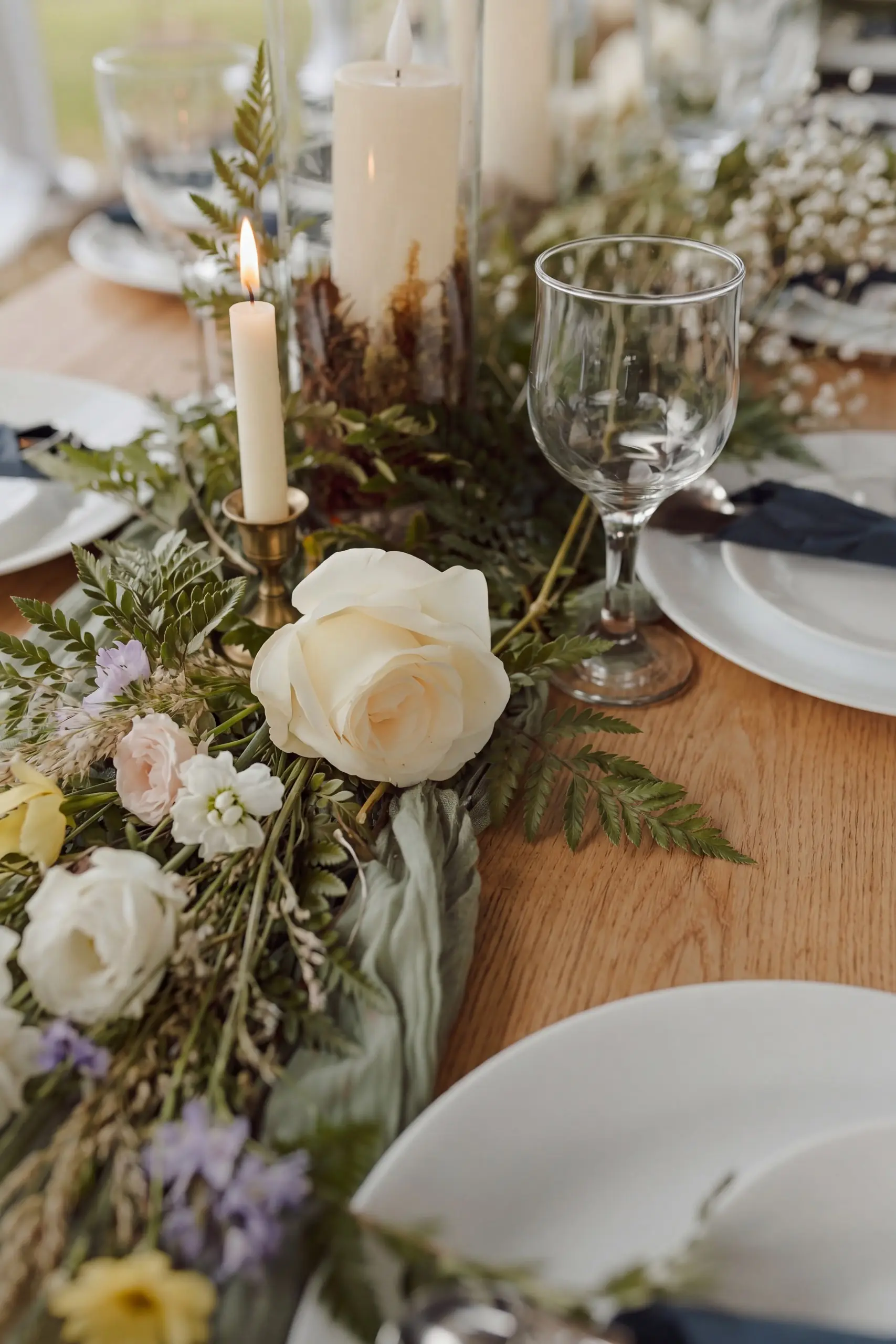 White roses, greenery and candles on a long wooden table in the hangar