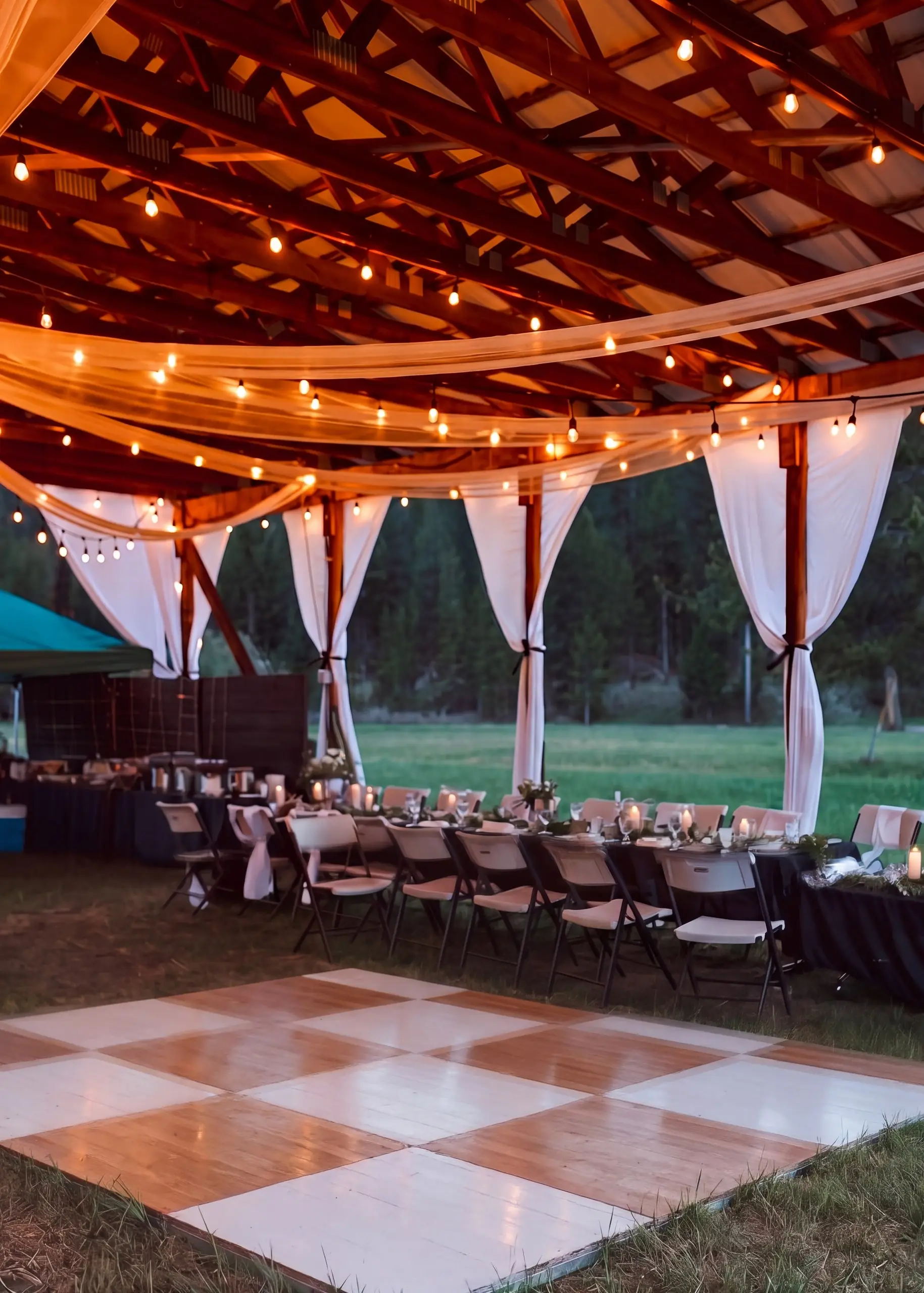 A checkered dance floor beside long tables under the hangar string lights and drapes